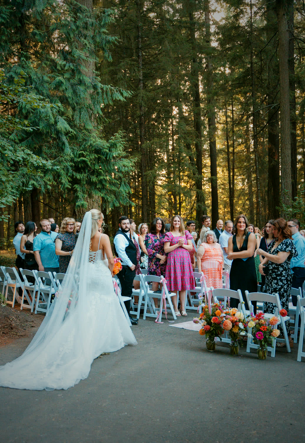 A bride at the top of the forest aisle, guests standing on both sides