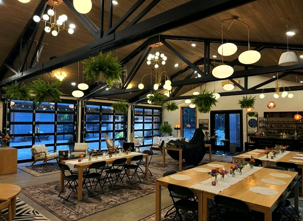 The hall in the evening, tables laid under hanging ferns and glass doors to the trees