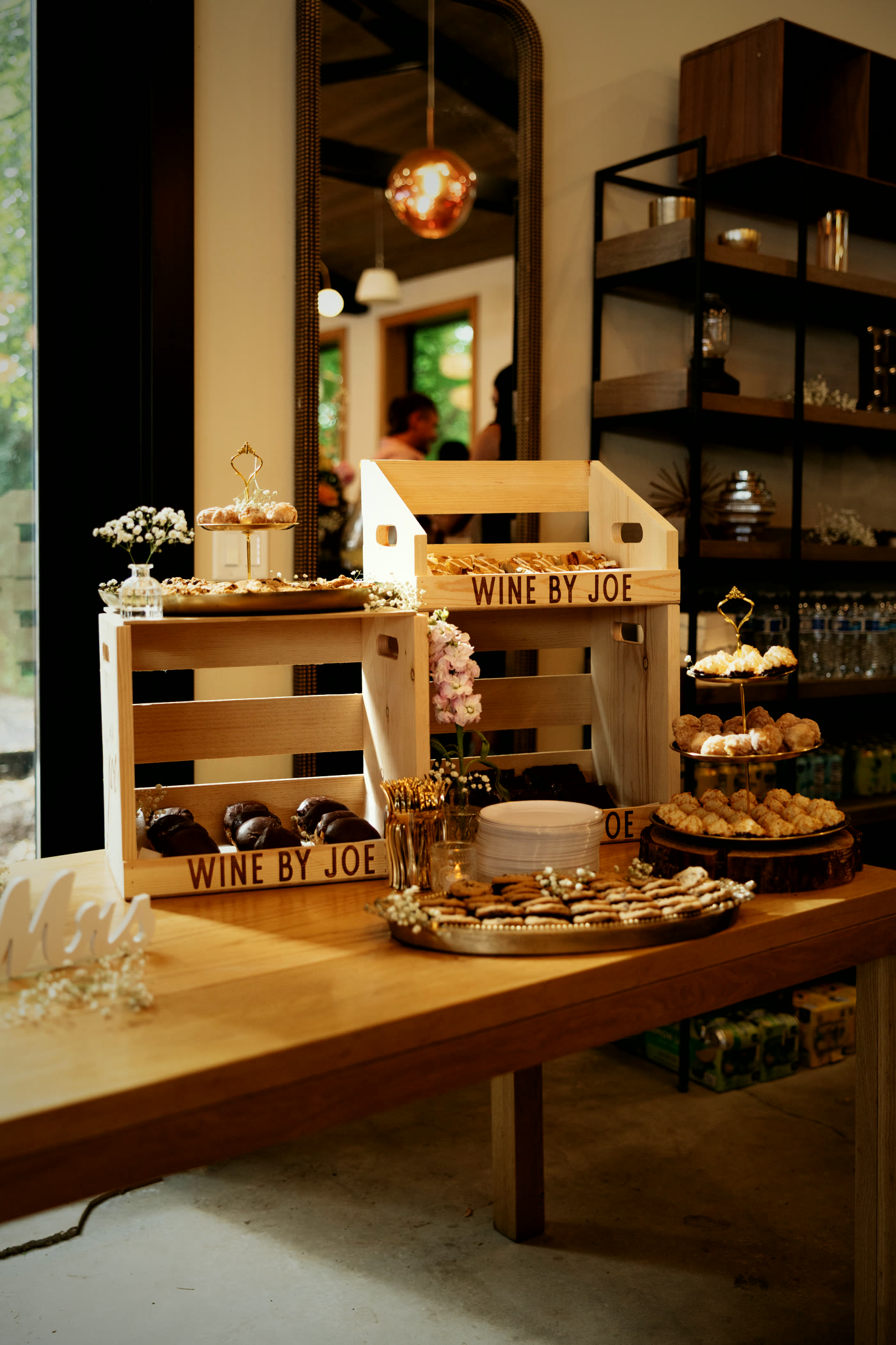 The hall in daylight: cream walls, light wood tables, black shelving and glass to the trees